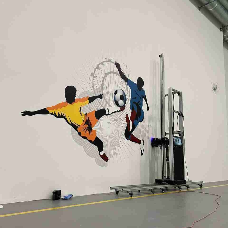 A large mural of two soccer players competing for a ball, printed directly onto a warehouse wall beside the printer that produced it